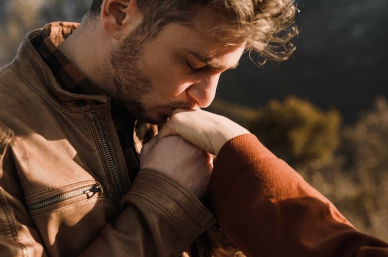 Young man kissing girlfriend hand in hilly sunny nature